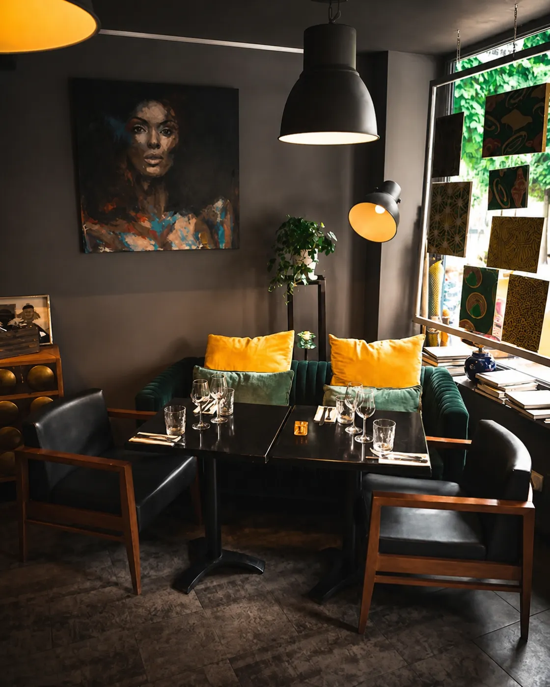 Le salon : banquette de velours vert, coussins jaunes et tables dressées sous un portrait peint